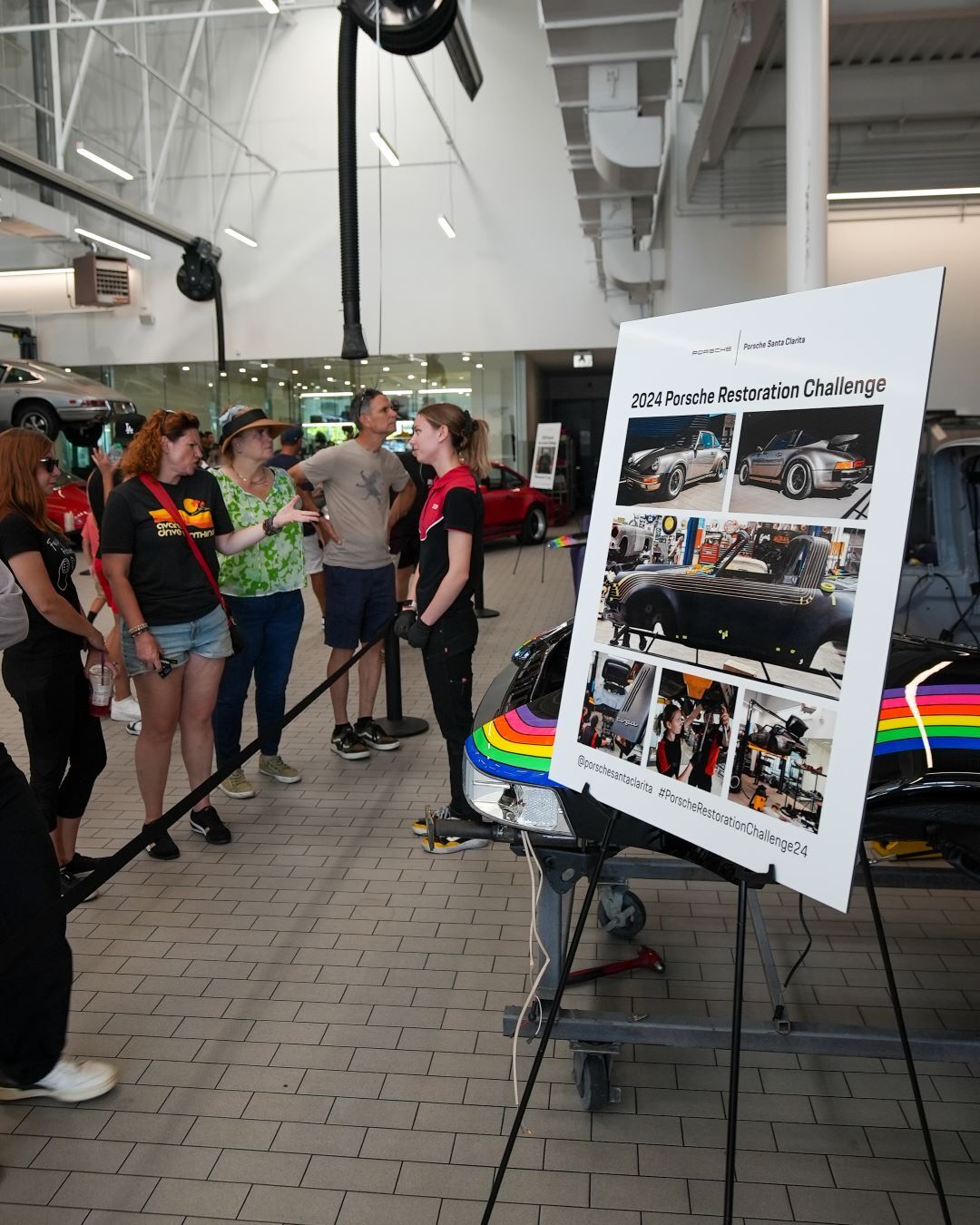 Group of people looking at a display board for the 2024 Porsche Restoration Challenge in a garage.