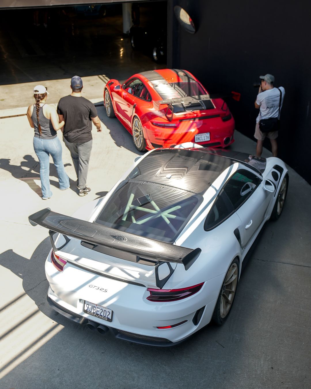 Overhead view of two Porsche GT3 RS sports cars, one white and one red, with four people nearby.