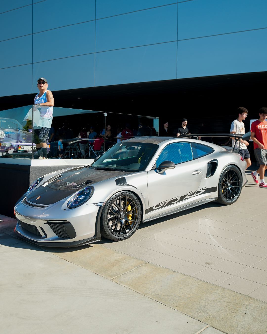 A silver Porsche GT3 RS sports car with a carbon fiber hood, black wheels, and yellow brake calipers, parked outdoors.