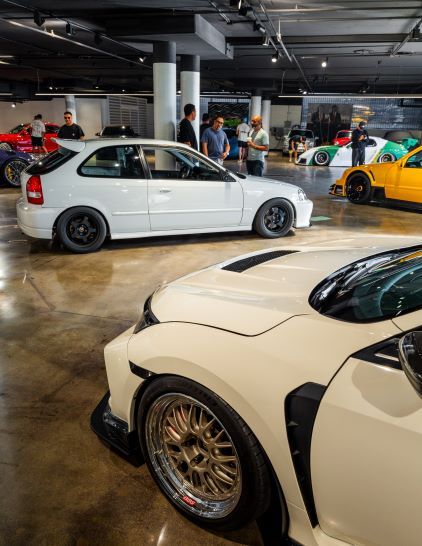 Several people examine modified cars displayed in a large, brightly lit showroom.