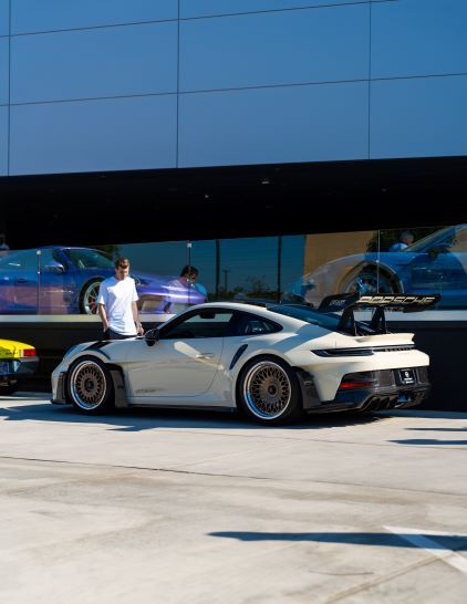 A man stands next to a white Porsche 911 GT2 RS parked in front of a modern building.