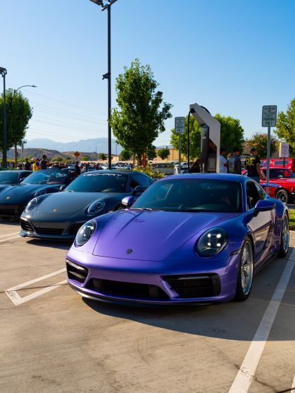 Several sleek, dark-colored sports cars are parked in a lot on a sunny day.