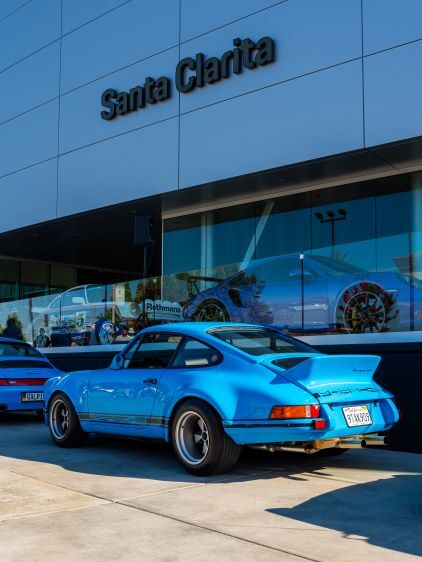 A blue Porsche sits parked in front of a building with 'Santa Clarita' signage.