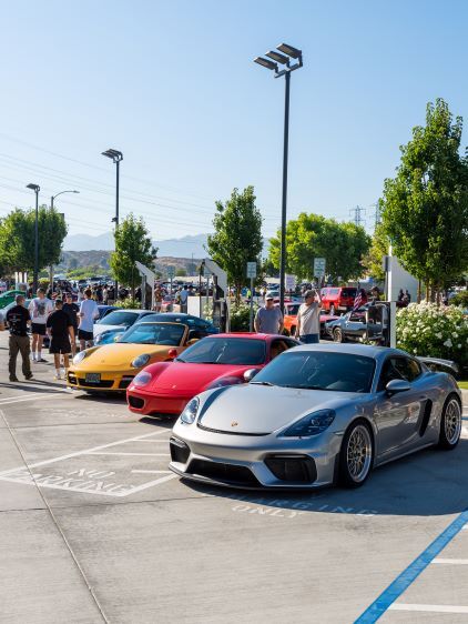 Several luxury sports cars, including yellow, red, and gray Porsches, are displayed at an outdoor car show.