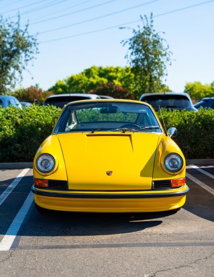 A bright yellow vintage Porsche convertible sits in a parking space, facing the camera.