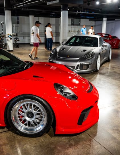 Several people view a display of luxury sports cars in a modern, spacious showroom.
