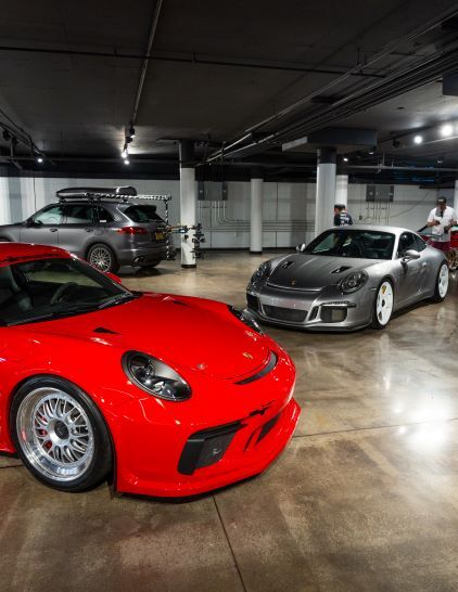 Several luxury cars, including red and gray Porsches, are parked in a spacious, dimly lit garage.
