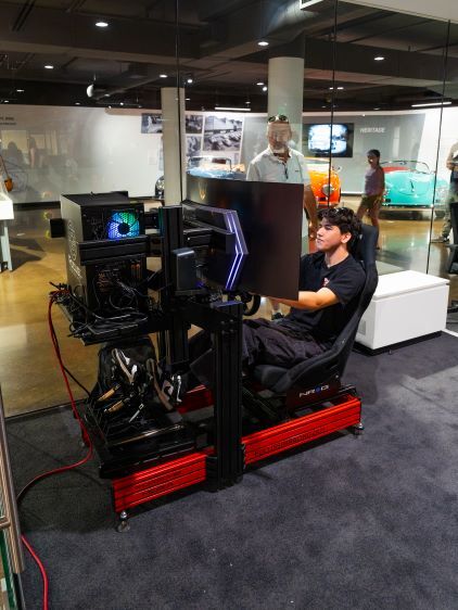 A young man sits in a racing simulator, focused on the screens and controls in front of him.