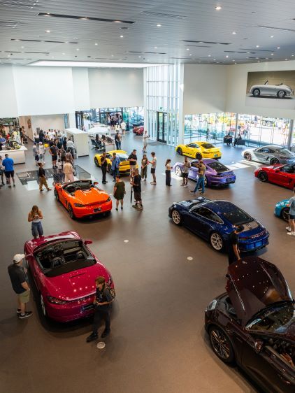 Visitors admire a large collection of luxury cars displayed in a modern showroom.