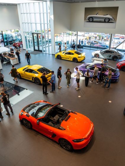 People explore a modern car dealership with several brightly colored sports cars on display.