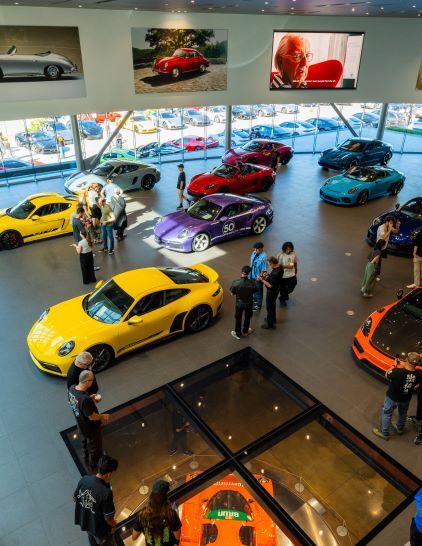 Several luxury cars are displayed in a modern showroom with people looking at them from above.