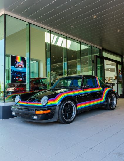A black Porsche with colorful rainbow stripes sits in a modern glass building.