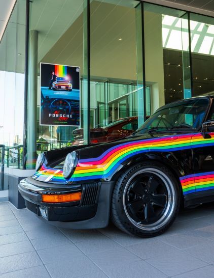 A black Porsche 911 with rainbow stripes sits on display in a modern showroom.