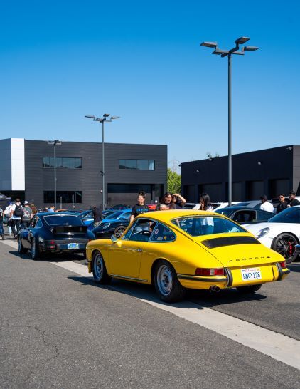 Vintage Porsche cars are displayed at an outdoor car show under a bright blue sky.