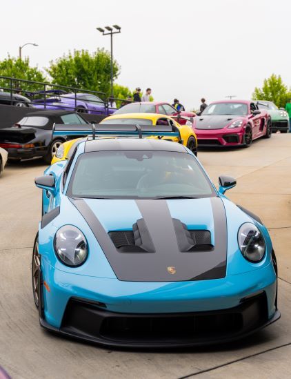 A bright blue Porsche with black racing stripes on the hood leads a line of colorful sports cars.