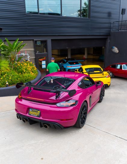 A hot pink sports car in the foreground with a yellow and a blue sports car parked in the background garage.