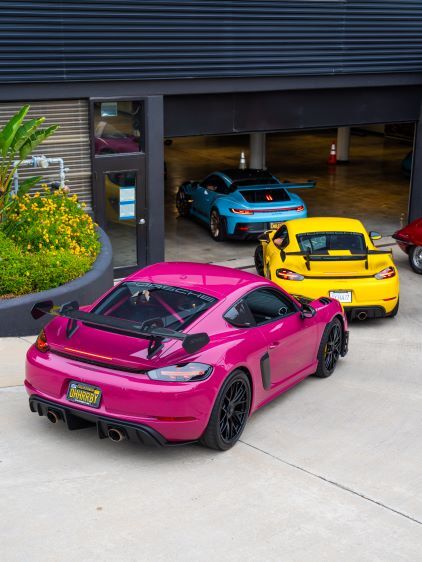 Rear view of a bright pink Porsche sports car with a large spoiler and silver wheels, in a garage.