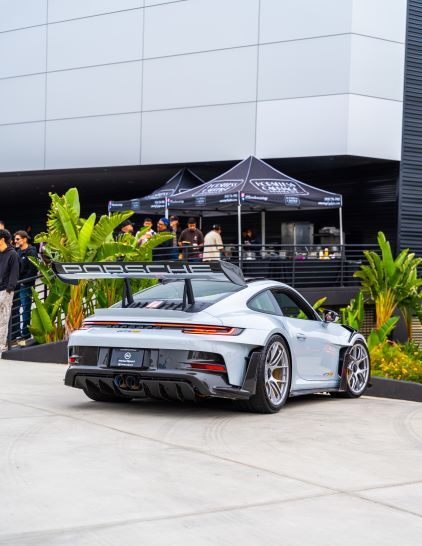 Rear view of a light gray Porsche GT3 RS with a wide spoiler, parked outside a modern building.
