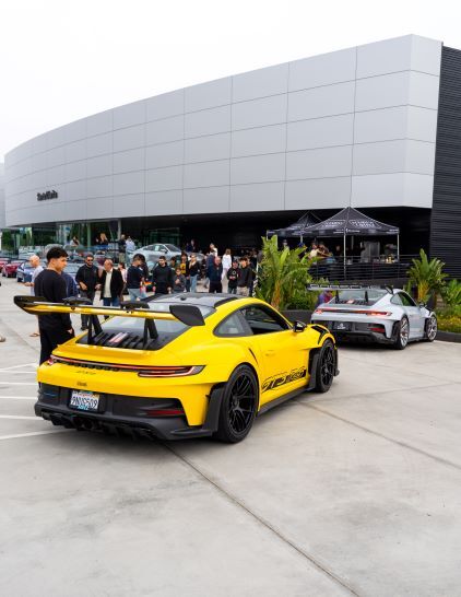 A bright yellow Porsche 911 GT3 RS with a large spoiler in a parking lot, a silver Porsche behind it.