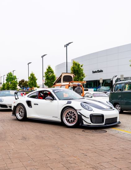 White Porsche GT2RS with red racing seats and custom livery parked on a brick street among other cars.