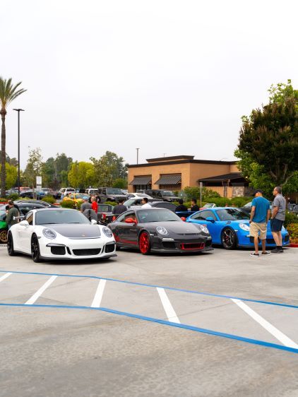 Several luxury sports cars are displayed in a parking lot with onlookers admiring them.