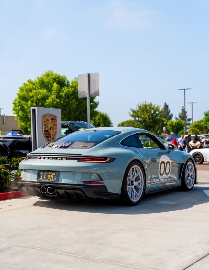 A silver Porsche 911 coupe sits in a parking lot with a racing number 00 on its rear.