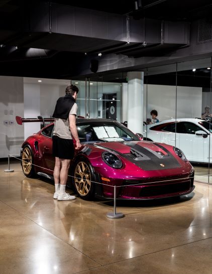 A person examines a red and black Porsche 911 GT3 RS displayed in a showroom.