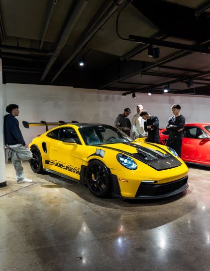 A bright yellow Porsche 911 GT3 RS stands on display as several people observe it.