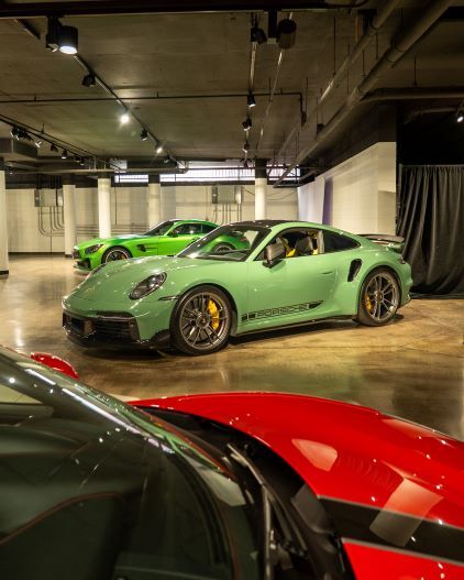 A bright green Porsche 911 sits in a well-lit garage alongside other luxury cars.