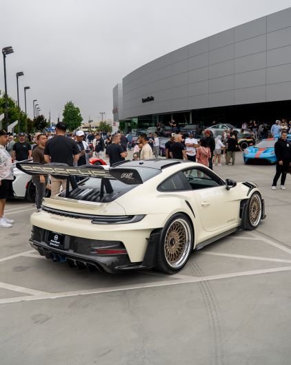 A white Porsche 911 GT3 RS sits in a parking lot surrounded by onlookers and other vehicles.