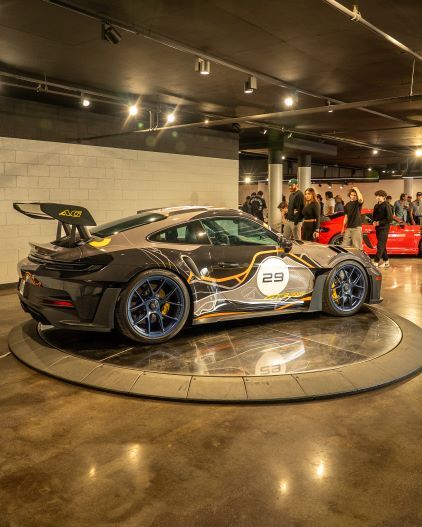 A white and gray Porsche 911 GT2 RS stands on a rotating platform in a showroom.
