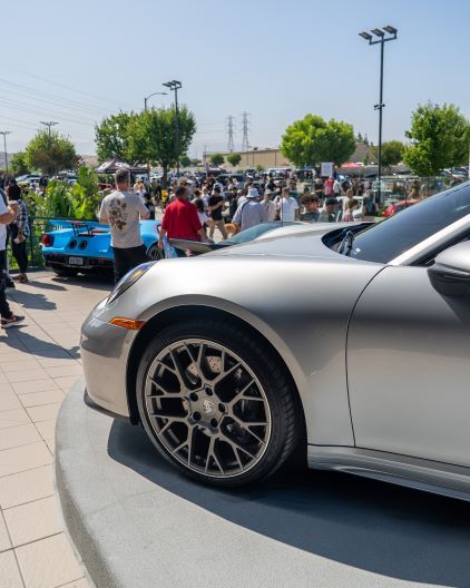 A gray Porsche sits at a car show with a crowd of people observing the vehicles.