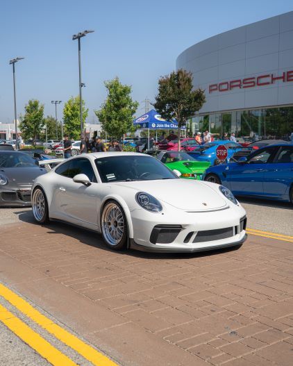 A white Porsche sports car is parked on a brick-paved area at a car show.