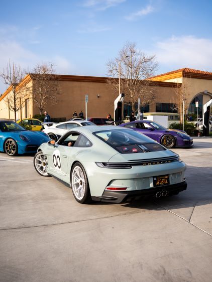 A light green Porsche 911 with racing number 00 sits parked amidst several other sports cars.