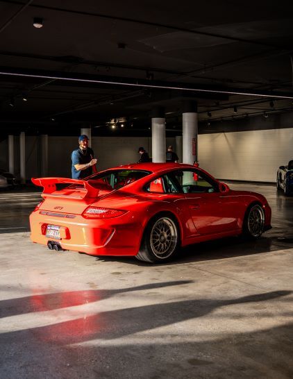 A pale blue Porsche with a black racing stripe on the hood is parked in a showroom.