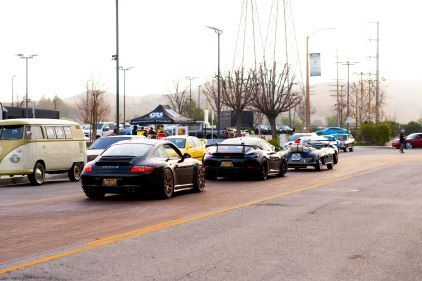 Classic and modern sports cars line up on a road at a car show.