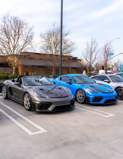 Two sports cars, one gray and one blue, are parked in a lot with a building in the background.