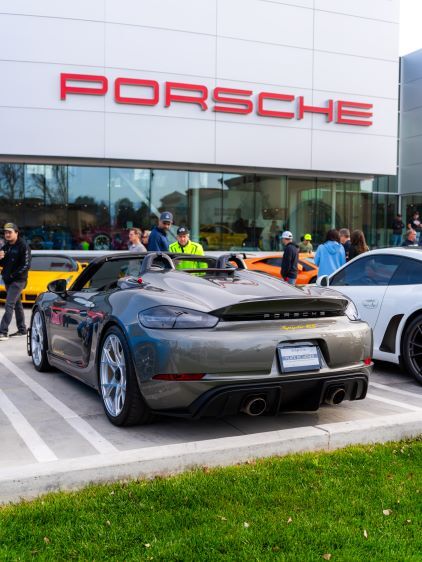 Grey Porsche convertible with a spoiler parked in front of a white building with the red 'PORSCHE' logo.