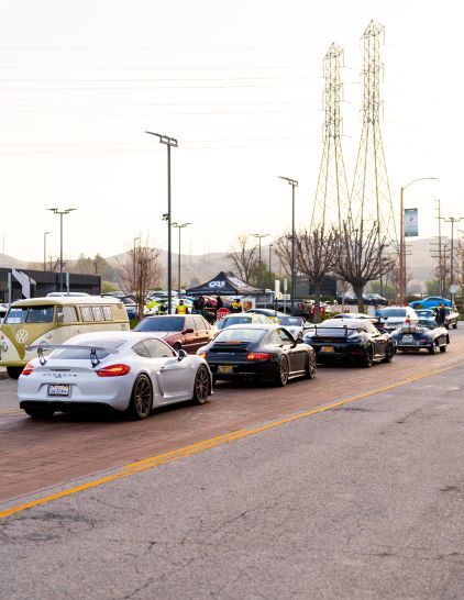 A line of modified sports cars is parked on a street at a car meet.