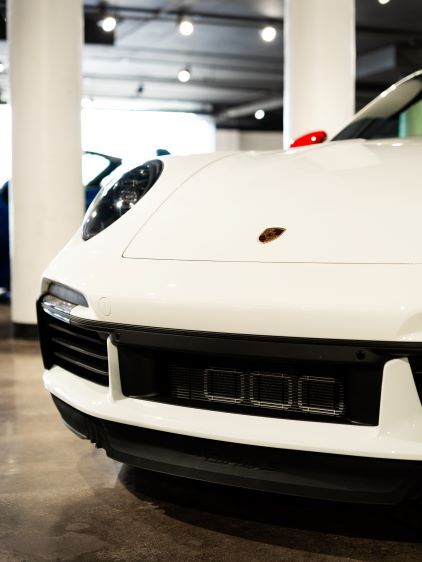 A white Porsche 911's front features a prominent black grille and emblem in a modern garage setting.