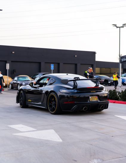 A black Porsche 911 GT3 parked in a lot with people and other cars in the background.