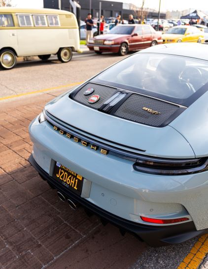 A light blue Porsche sits on a brick road at a car show, showcasing its rear design.