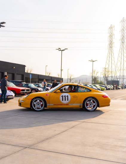 A yellow Porsche with number 111 is parked among several other cars at a car show.