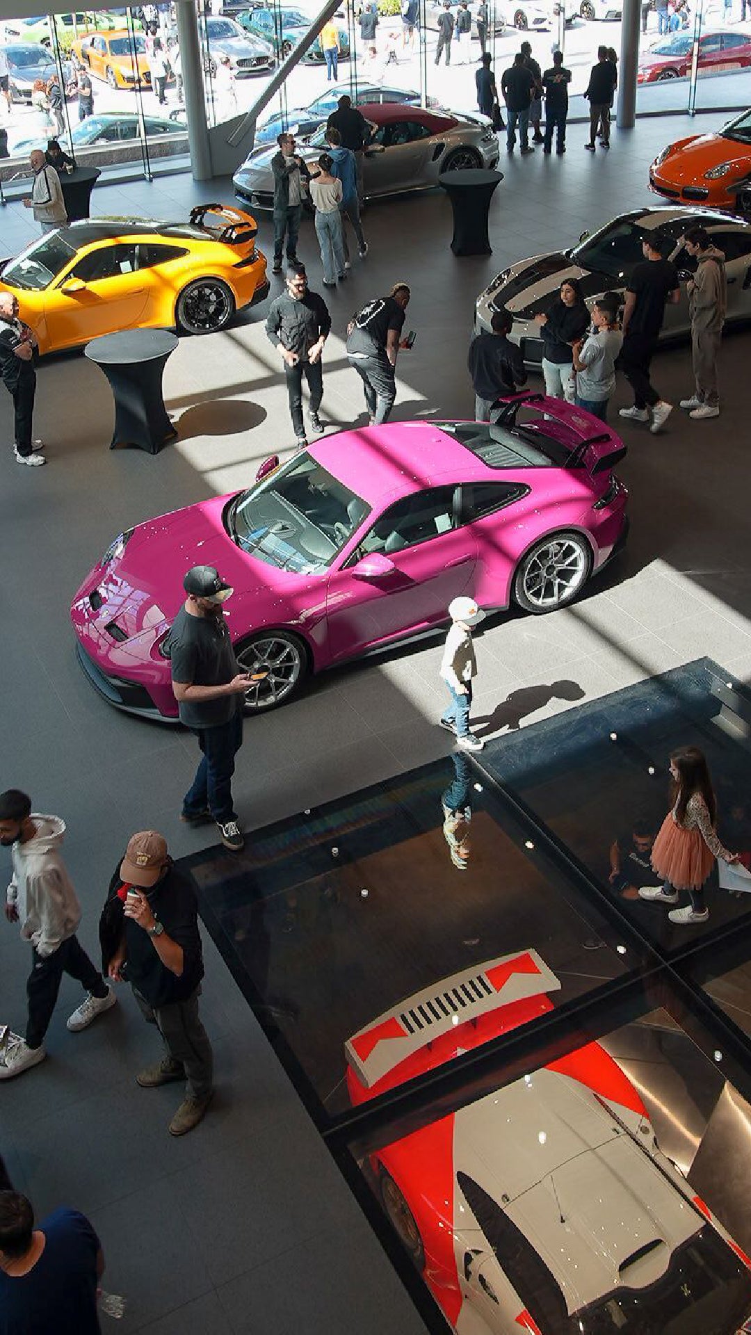 Overhead view of a crowded car dealership with a pink, an orange, and a white and red sports car.