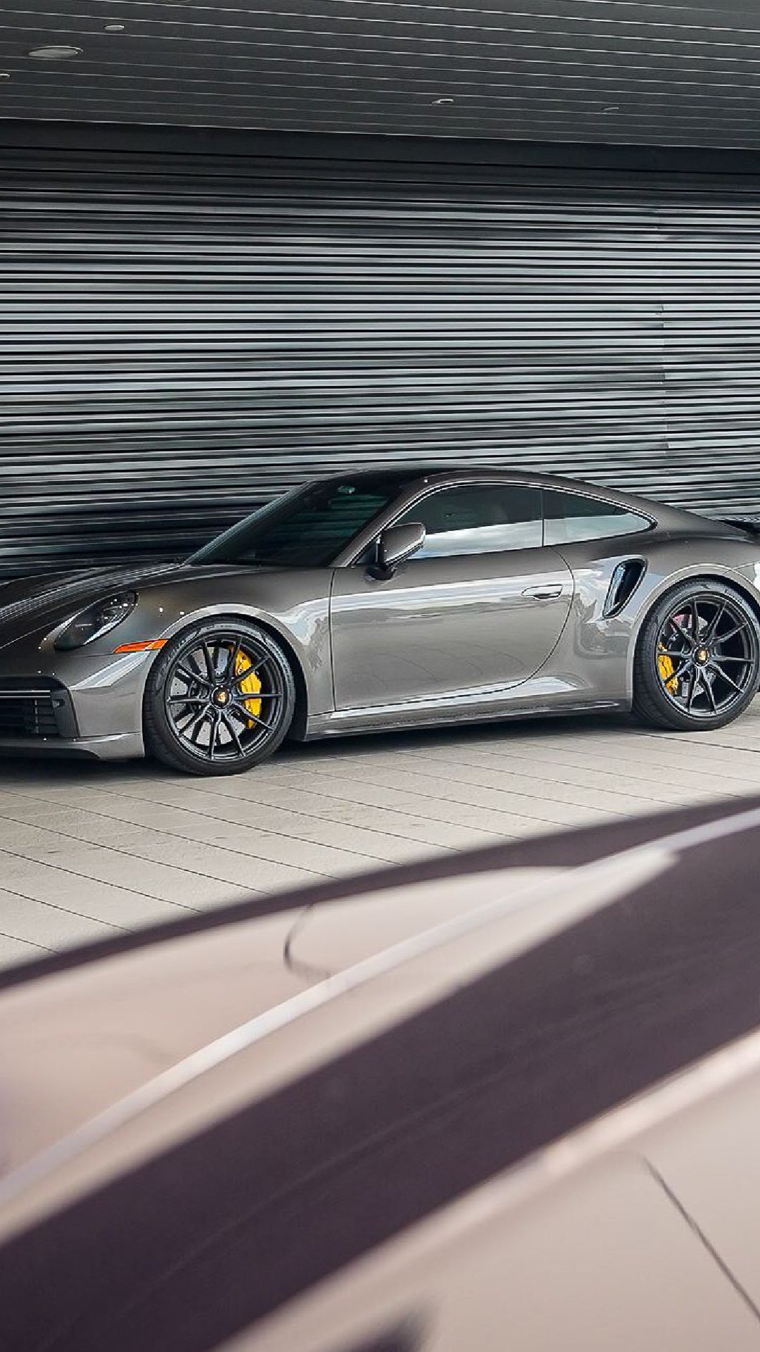 A grey Porsche 911 with yellow brake calipers parked indoors in front of a metal slatted wall.