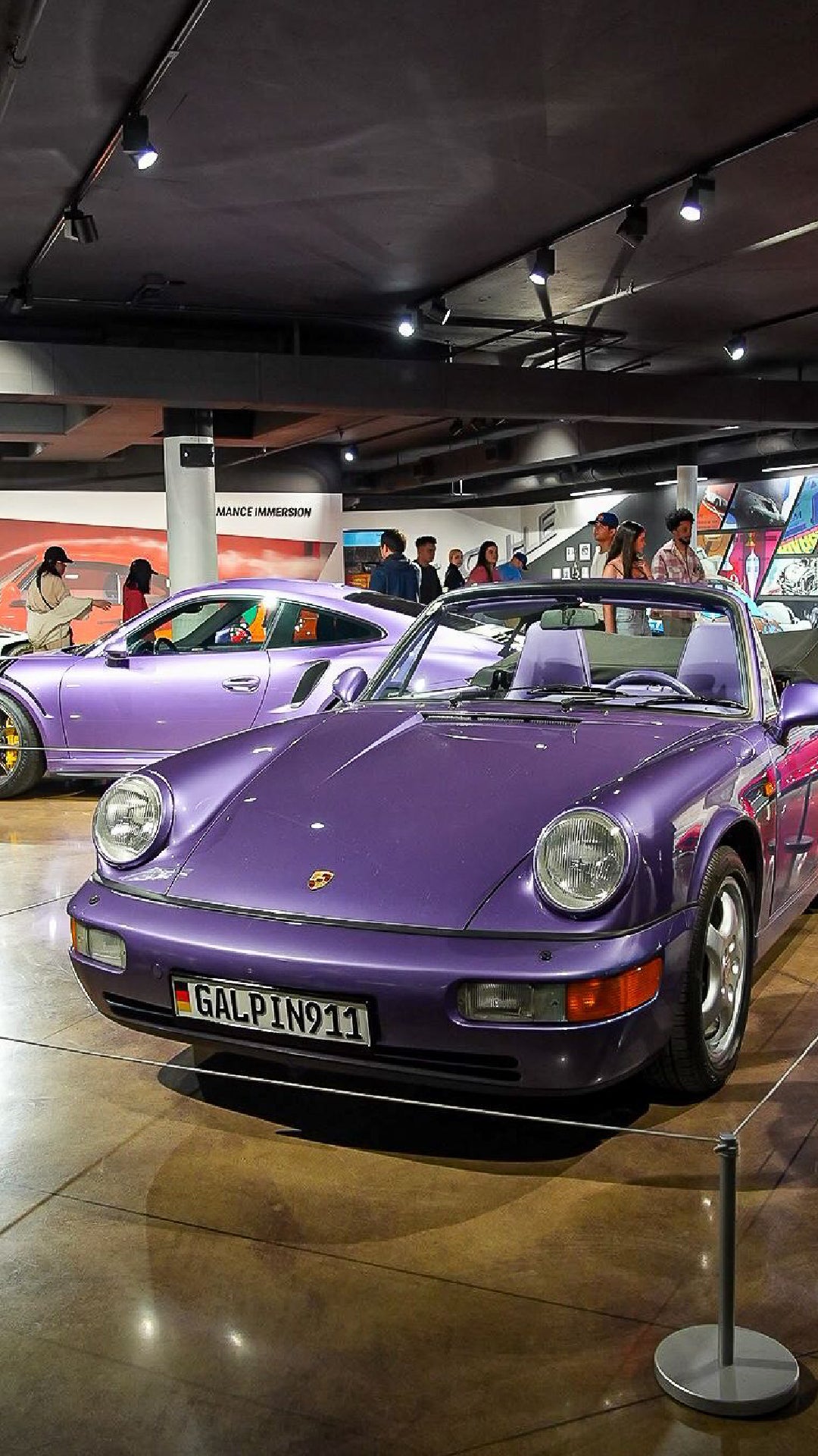 Two purple Porsche cars displayed in a showroom, with a convertible in the foreground and a coupe behind.