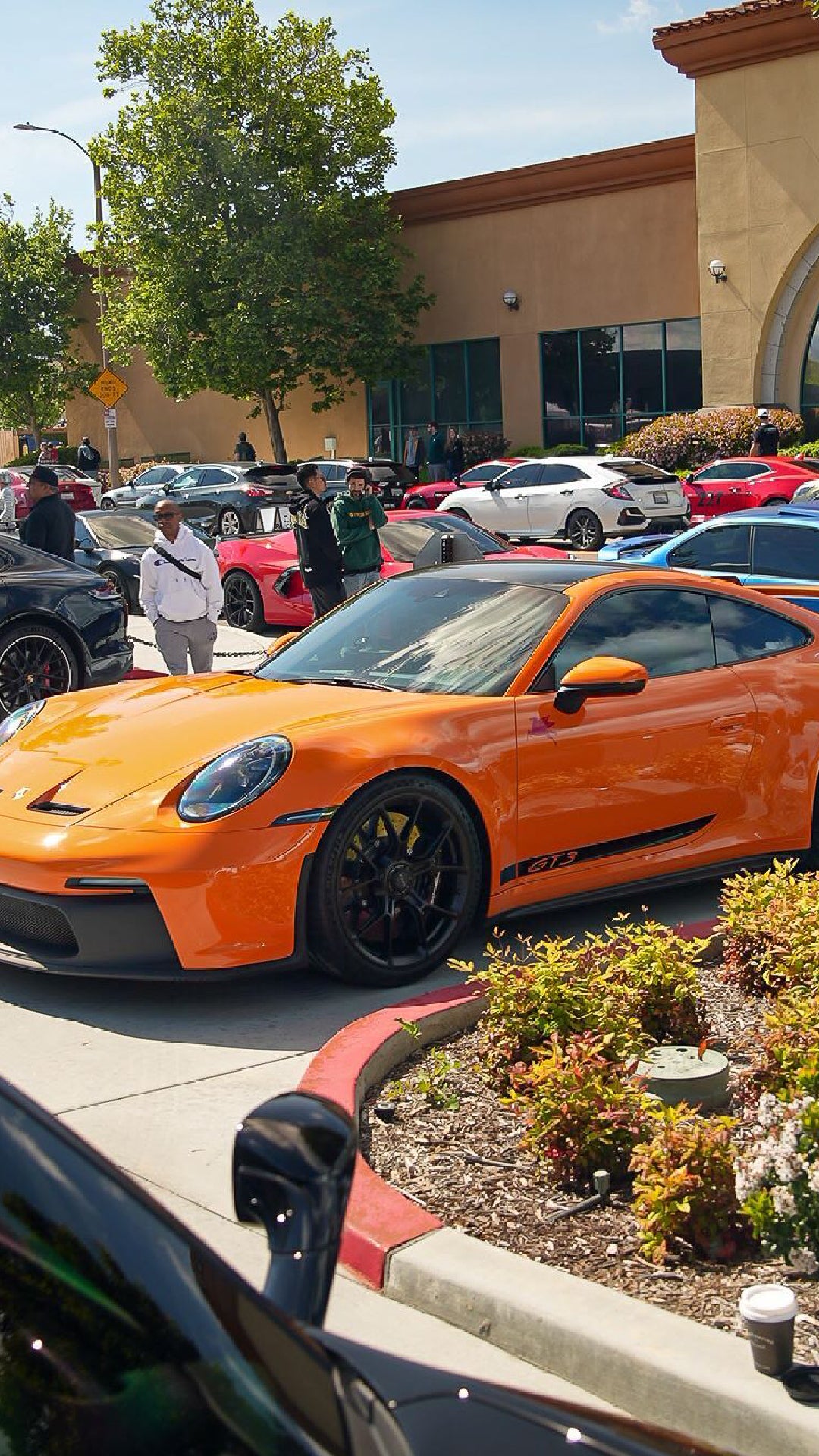 Bright orange Porsche GT3 sportscar parked at a car show with other vehicles and people in a parking lot.