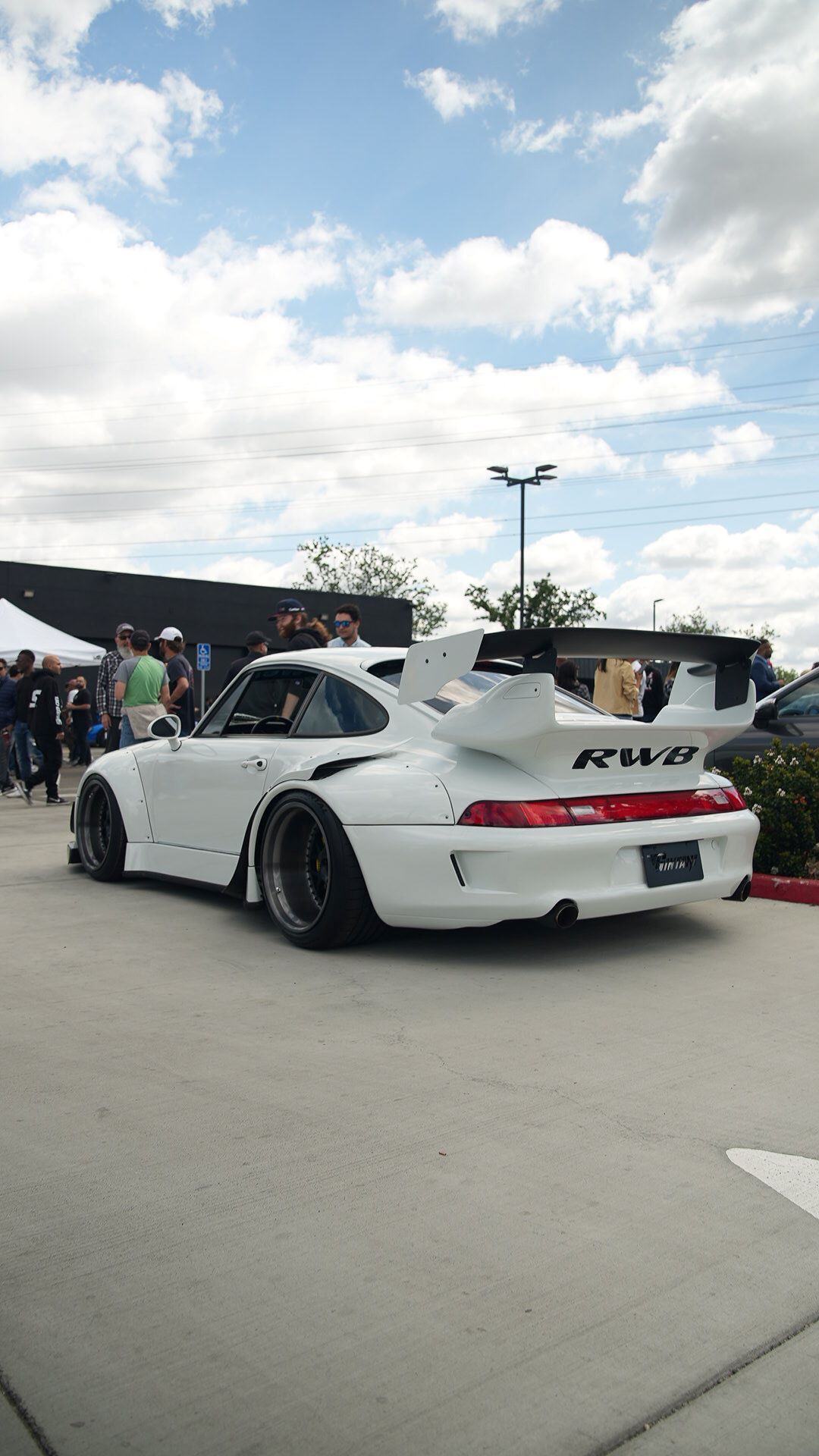 Rear view of a custom RWB widebody white Porsche 911 with a huge rear wing, parked outdoors.