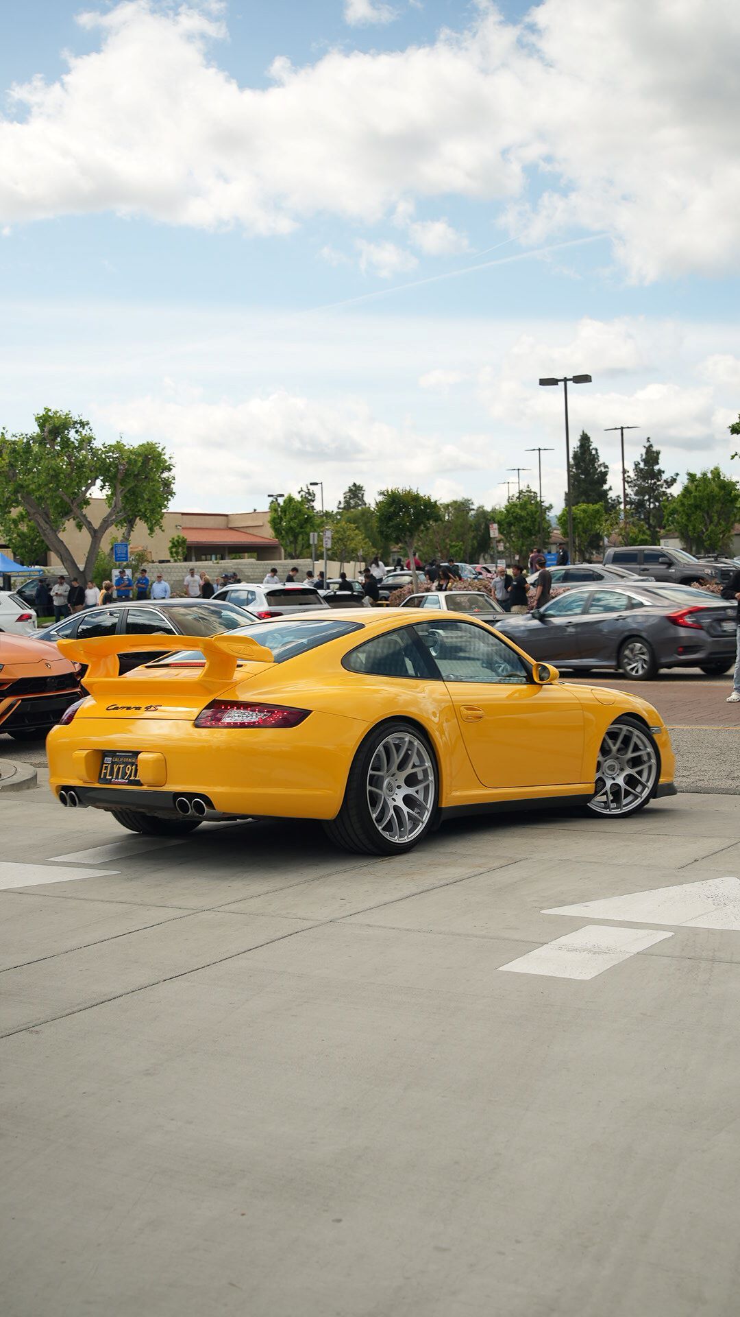 Bright yellow Porsche 911 Carrera GTS parked at an outdoor car show under a cloudy sky.
