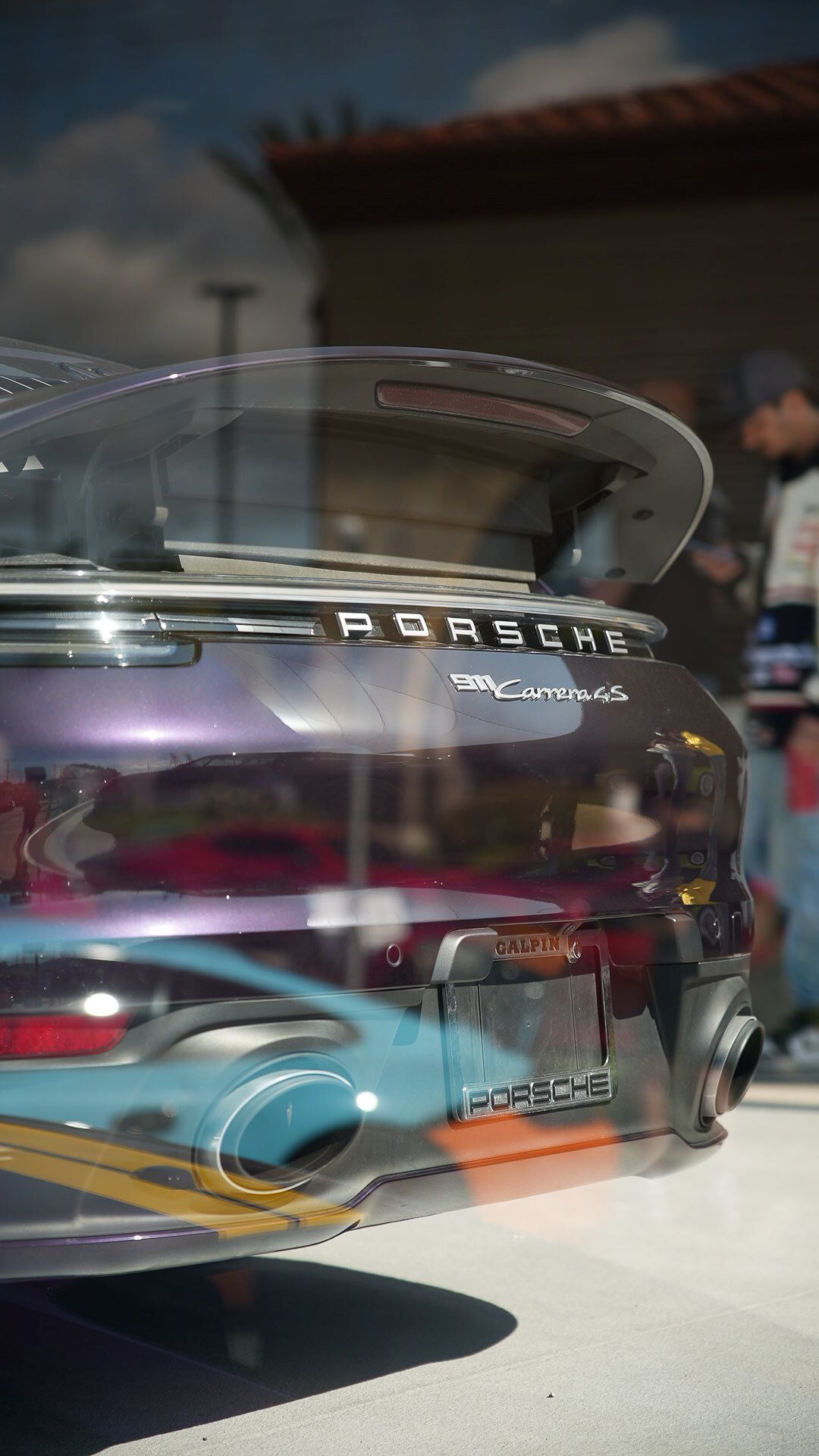 Rear-view of a metallic purple Porsche 911 Carrera 4s with a large spoiler, reflections on its shiny surface.